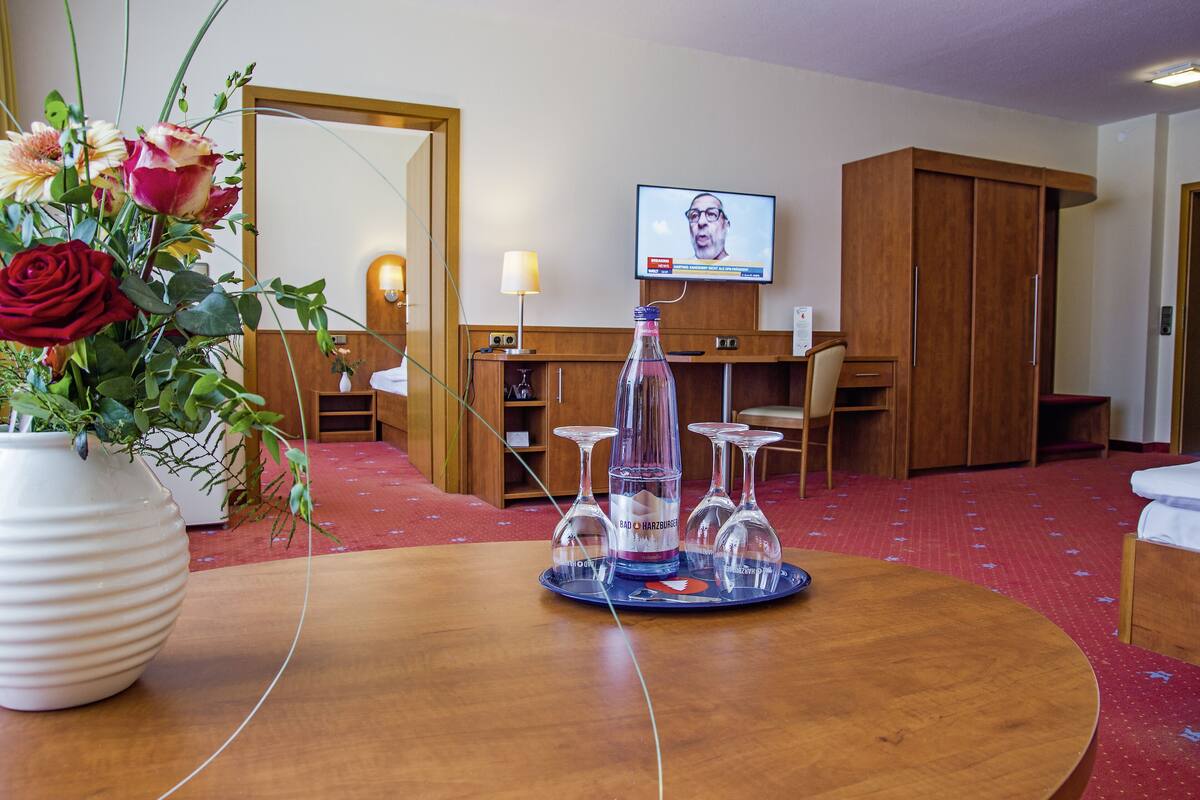 Une chambre d’hôtel avec une table en bois, un vase de fleurs, un téléviseur fixé au mur et une armoire.