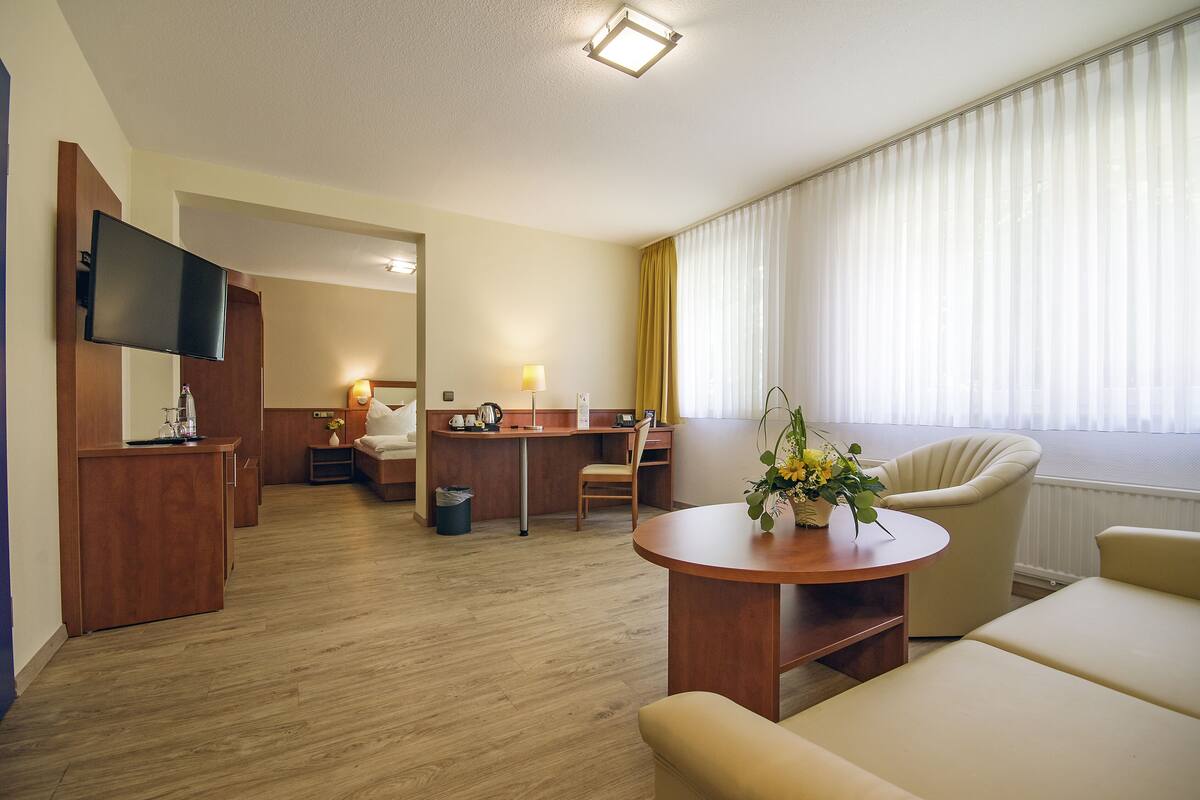 Une chambre d’hôtel équipée d’un bureau en bois, d’une télévision, d’un canapé et d’un coin repas avec une chaise et une table.