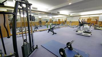 Een sportschool met fitnessapparatuur, spiegels en een blauwe mat.