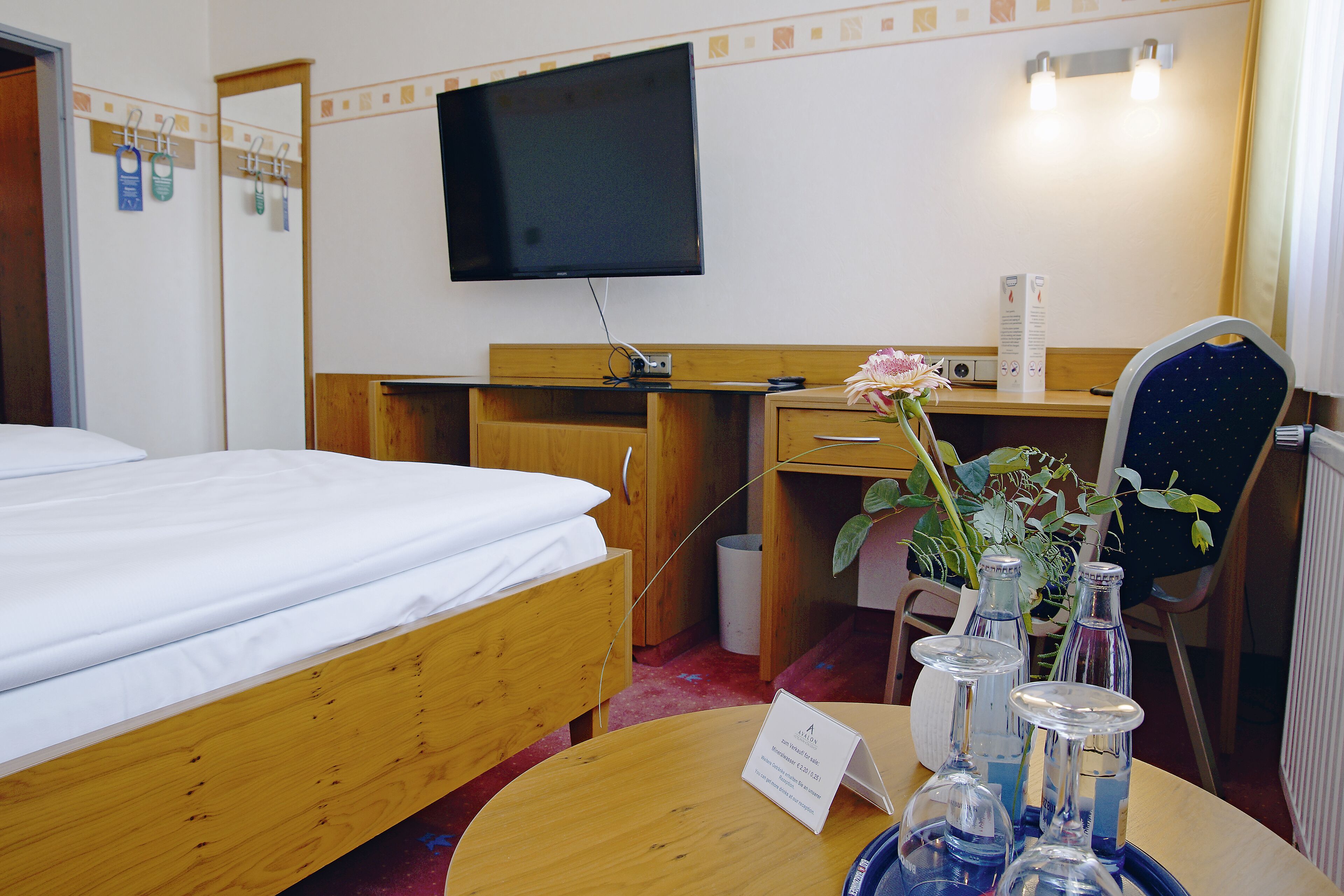 Ein Hotelzimmer mit einem Bett, einem Schreibtisch, einem Sessel, einem Fernseher und einem Tisch mit einer Vase und Flaschen.