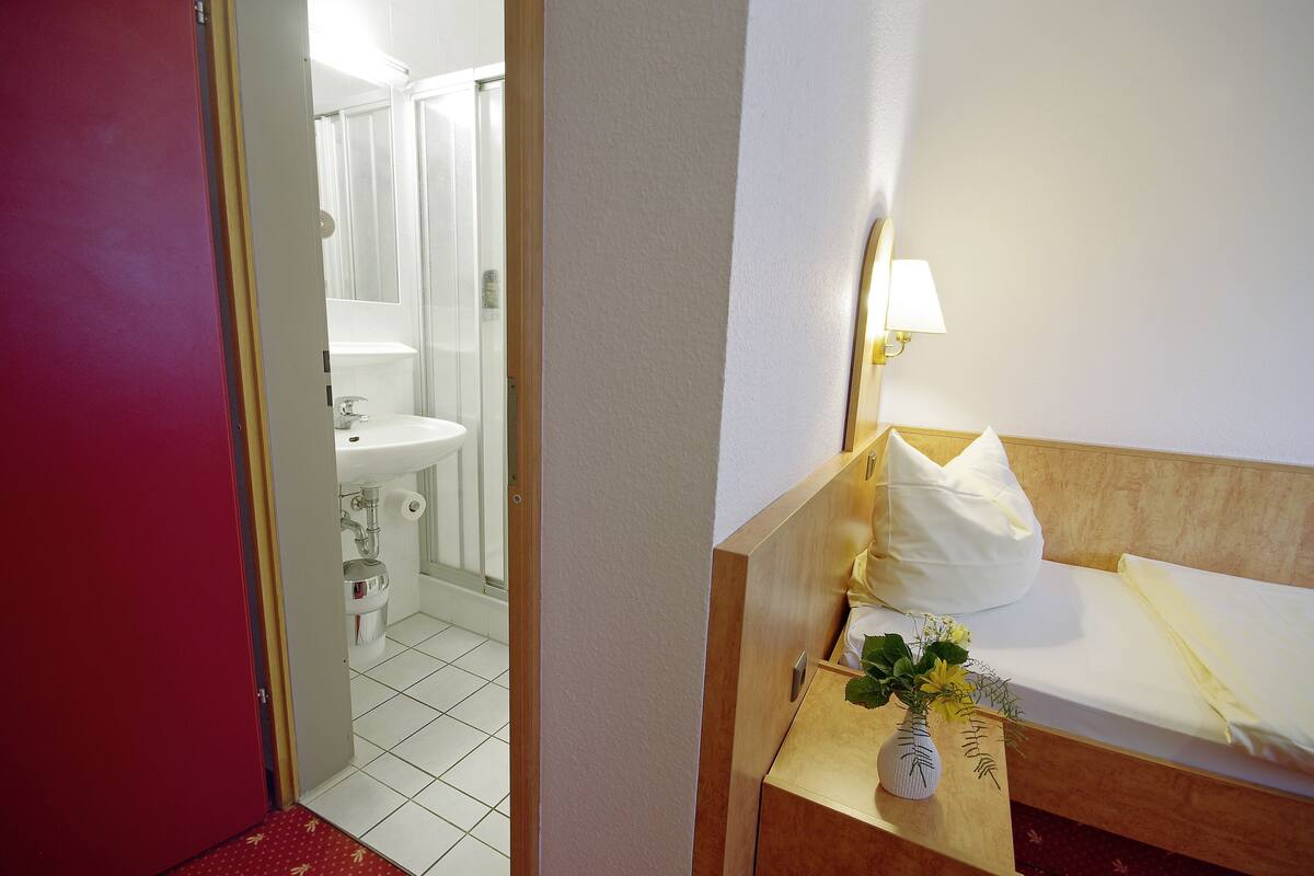 Une chambre d’hôtel avec un lit, une table de chevet avec une lampe, une petite plante et une vue sur la salle de bain.