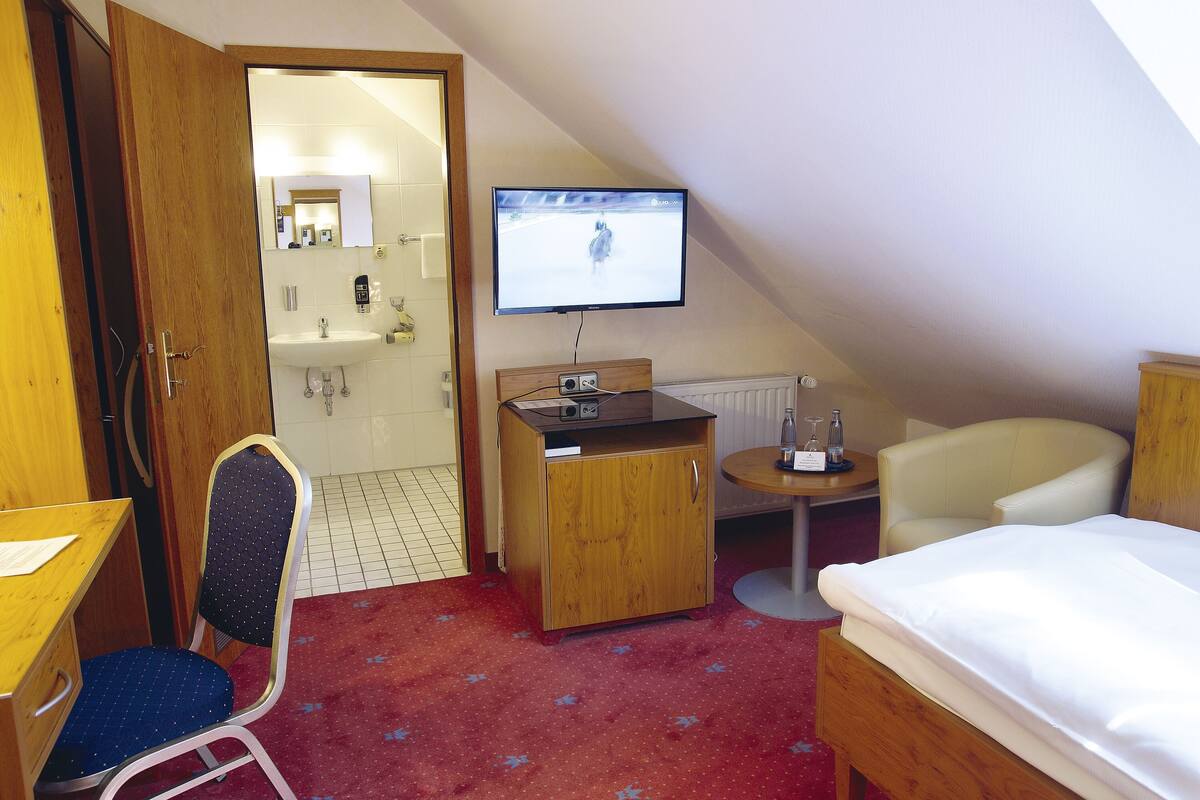 Une chambre d’hôtel comprenant un lit, un bureau, une chaise, une télévision et une petite table avec une bouteille et des verres.