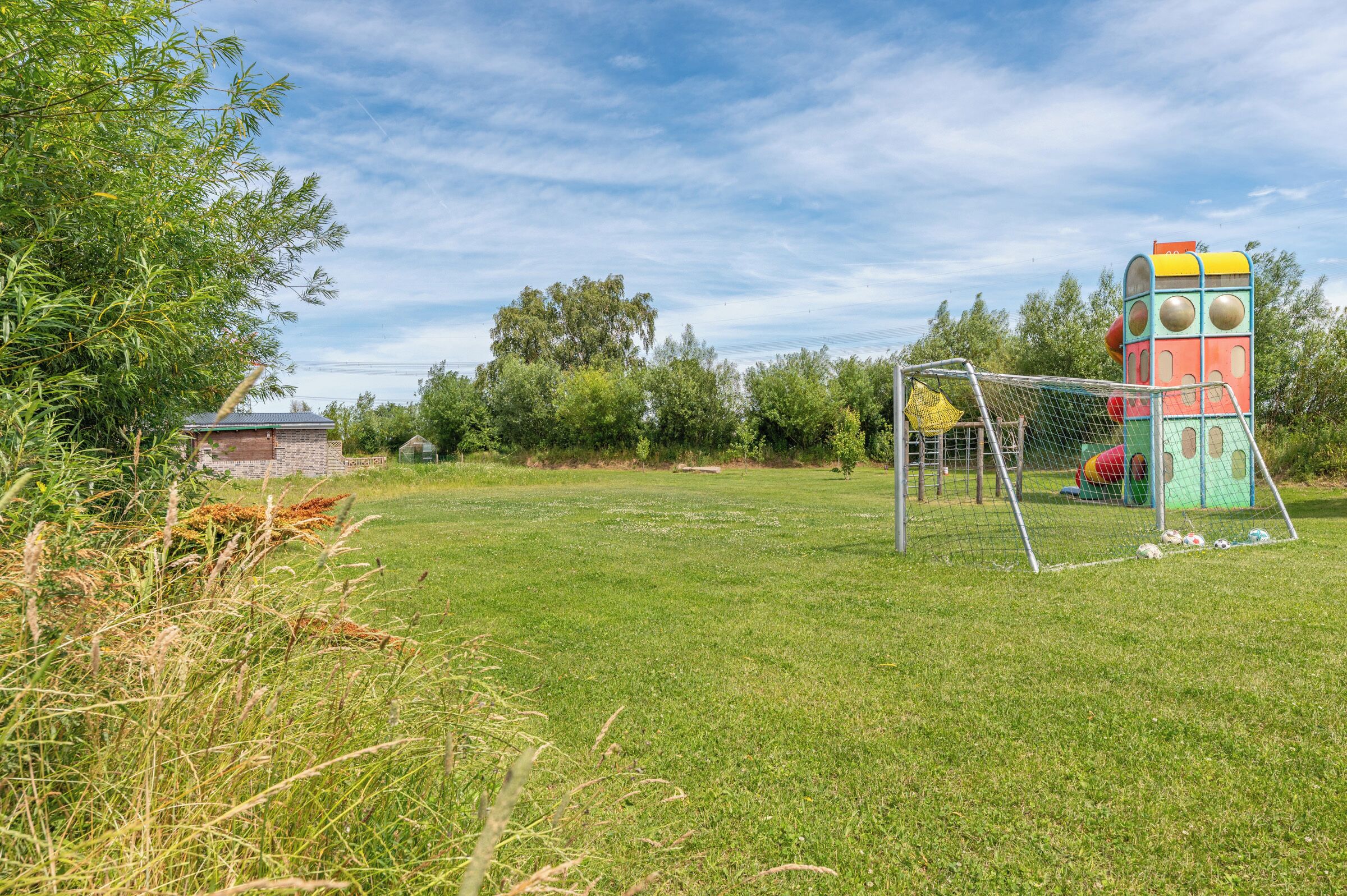 En græsplæne med en farverig legeplads og et fodboldmål.
