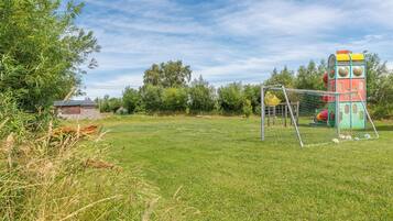 En græsplæne med en farverig legeplads og et fodboldmål.