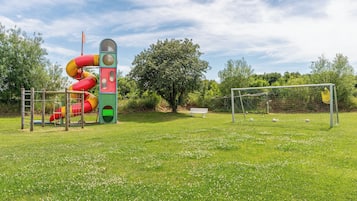 Une aire de jeux avec un toboggan, des structures d’escalade et un but de football.