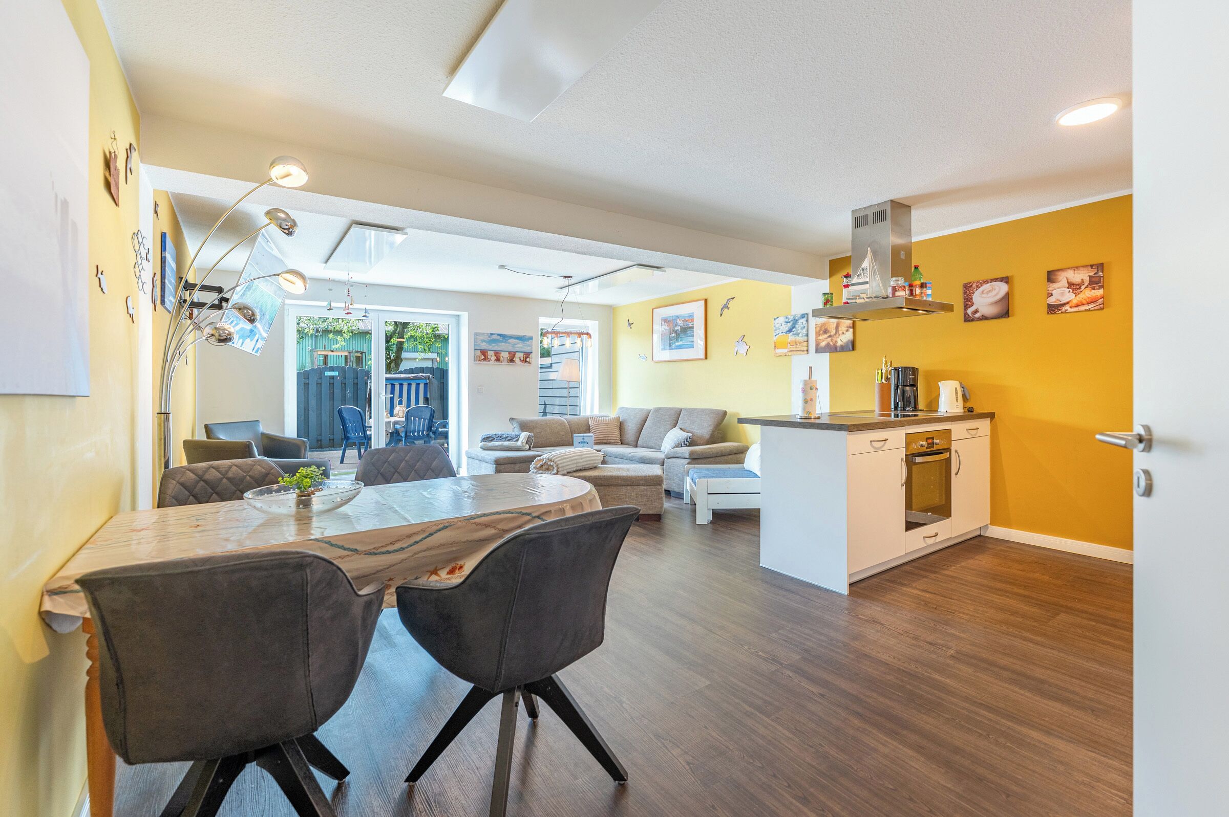 A modern living space with a dining area, sofas, a kitchen, and a view of the outdoors.