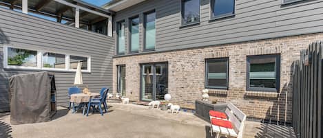 A modern two-story building with a patio area featuring outdoor seating and a barbecue grill.