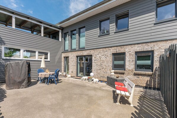 A modern two-story building with a patio area featuring outdoor seating and a barbecue grill.