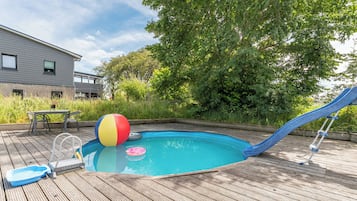 Une piscine avec un toboggan et un ballon de plage sur une terrasse en bois.