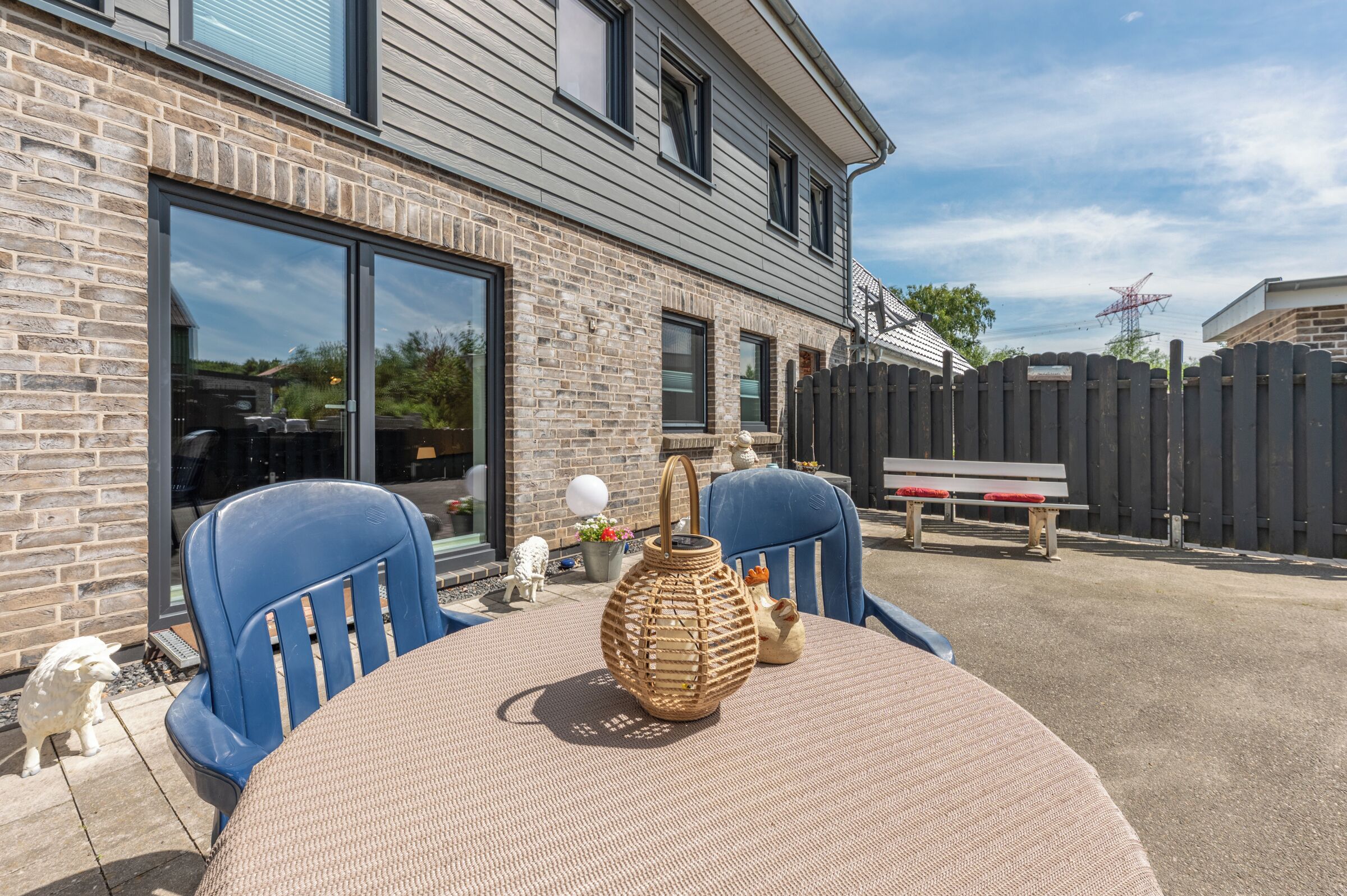 Une terrasse avec une table ronde, deux chaises bleues, un vase en osier et une clôture en bois.