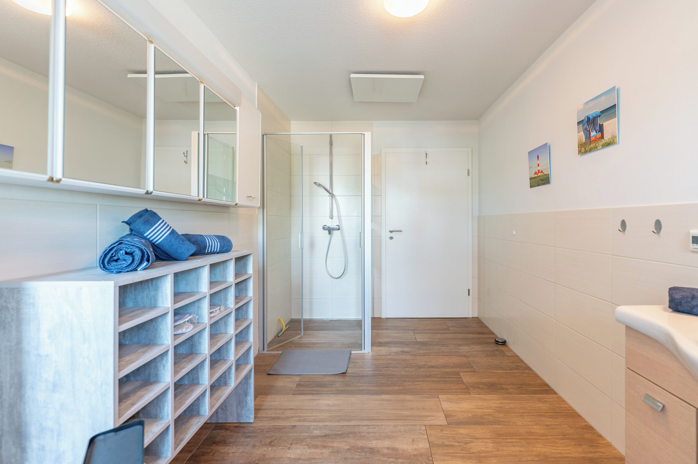 A modern bathroom with a shower, a towel rack, and a shelf with folded towels.