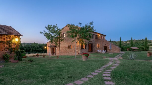 Une maison en briques avec un chemin pavé menant à l’entrée, entourée d’une pelouse bien entretenue et de plantes en pot.