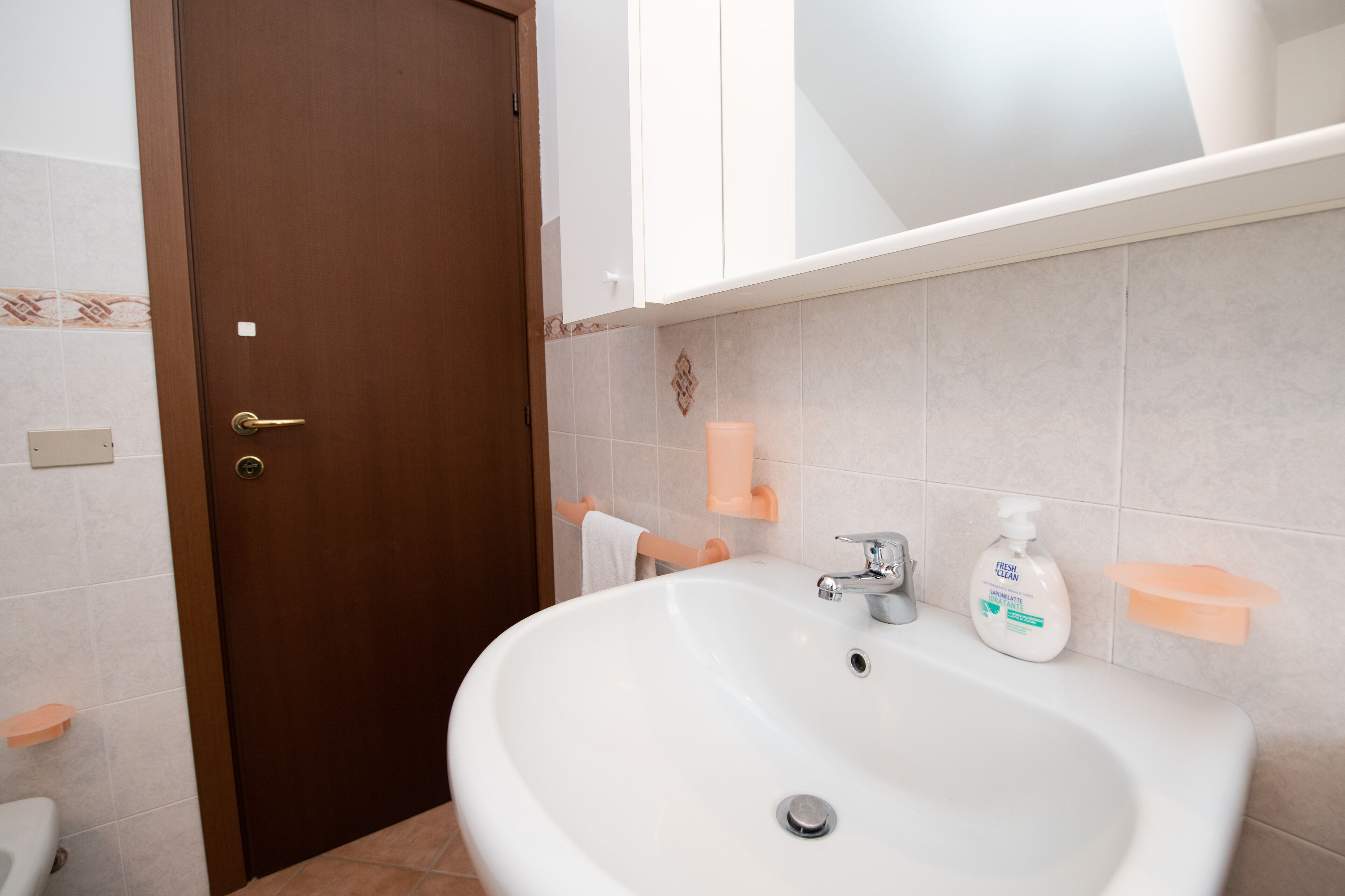 Ein Badezimmer mit weißem Waschbecken, Handtuchhalter, Seifenspender und Toilette.