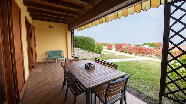 Un patio techado con mesa y sillas de madera, un banco y vistas a un jardín ajardinado.