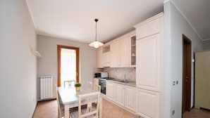 Una cocina con armarios blancos, una mesa de comedor con sillas, una lámpara colgante y una ventana con cortinas.