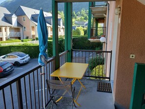 A balcony with a yellow table and chairs, a blue umbrella, and a view of houses and greenery.