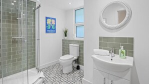 Badeværelse med brusekabine, toilet, håndvask med spejl og et vindue.