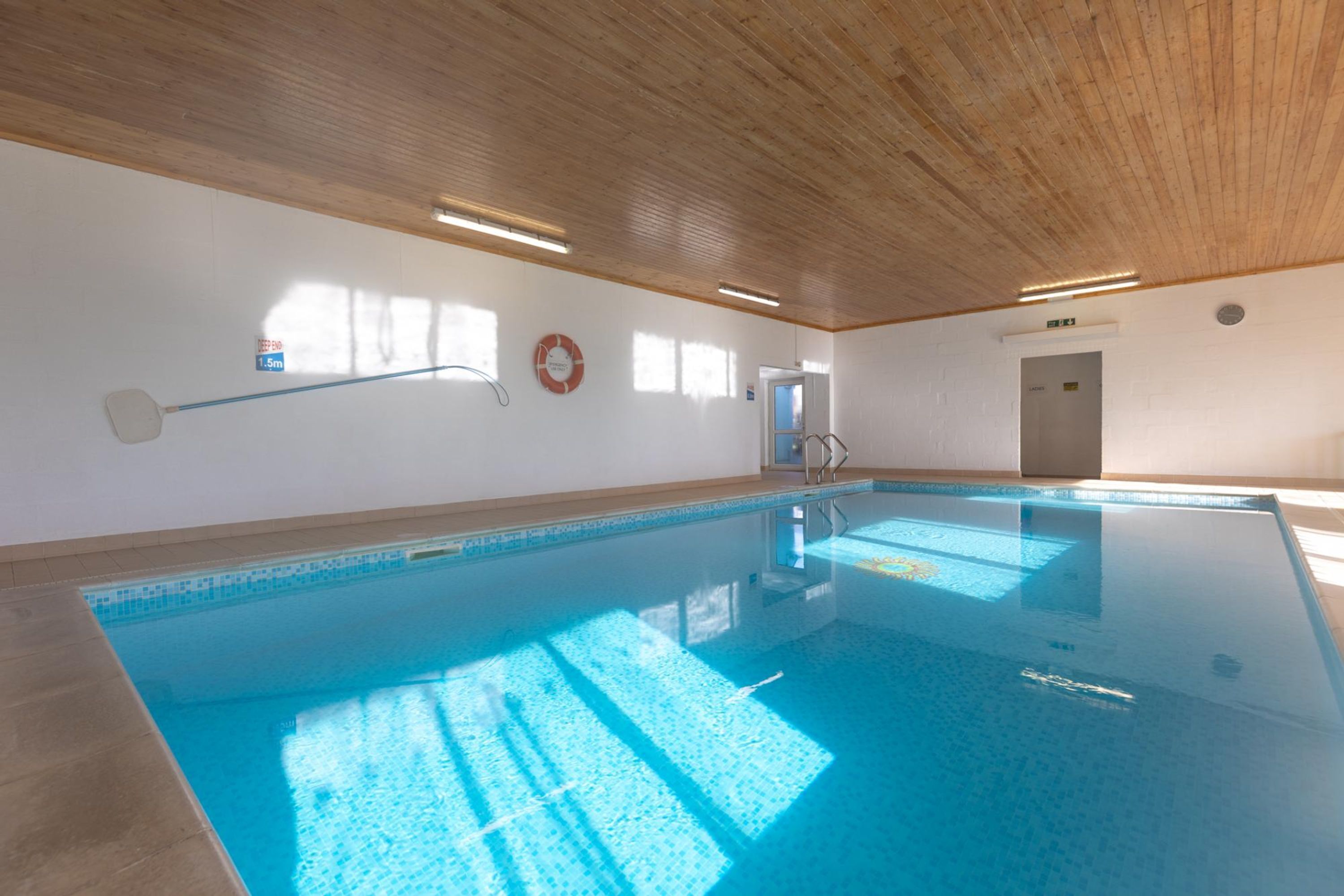 Una piscina interior con techo de madera, agua cristalina y un flotador en la pared.