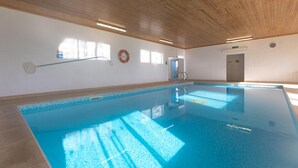 Una piscina interna con soffitto in legno, acqua cristallina e un galleggiante appeso alla parete.