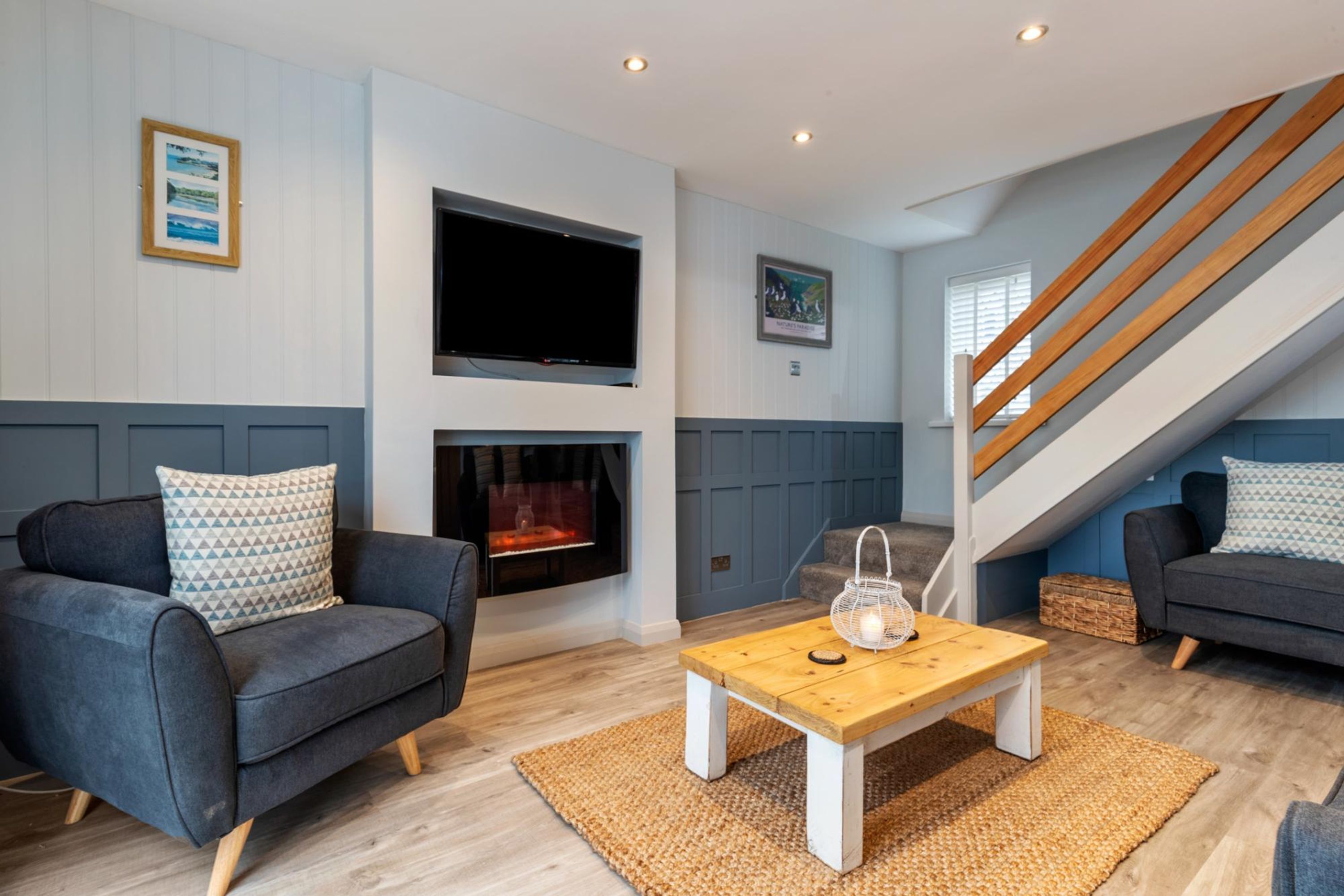 A modern living room with a fireplace, two sofas, a coffee table, and a staircase.