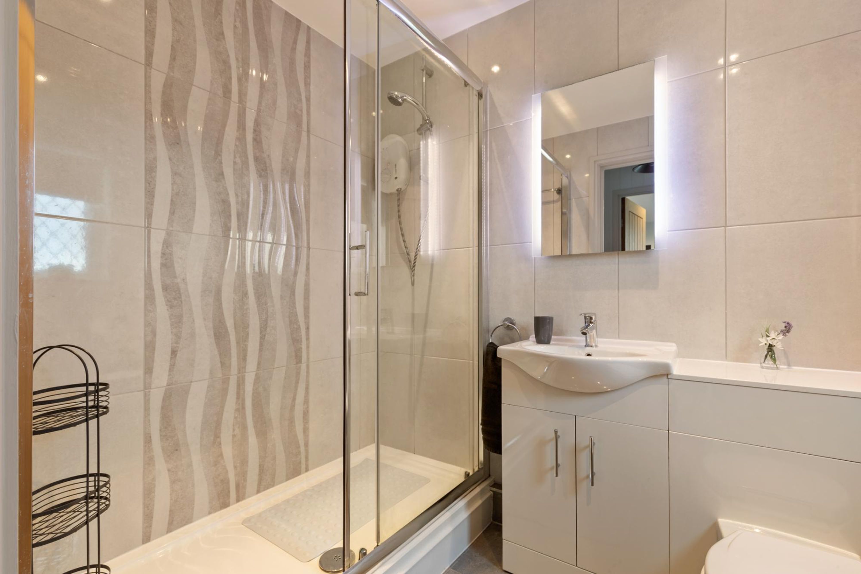 Un baño moderno con ducha envuelta en vidrio, un lavamanos blanco y un inodoro.