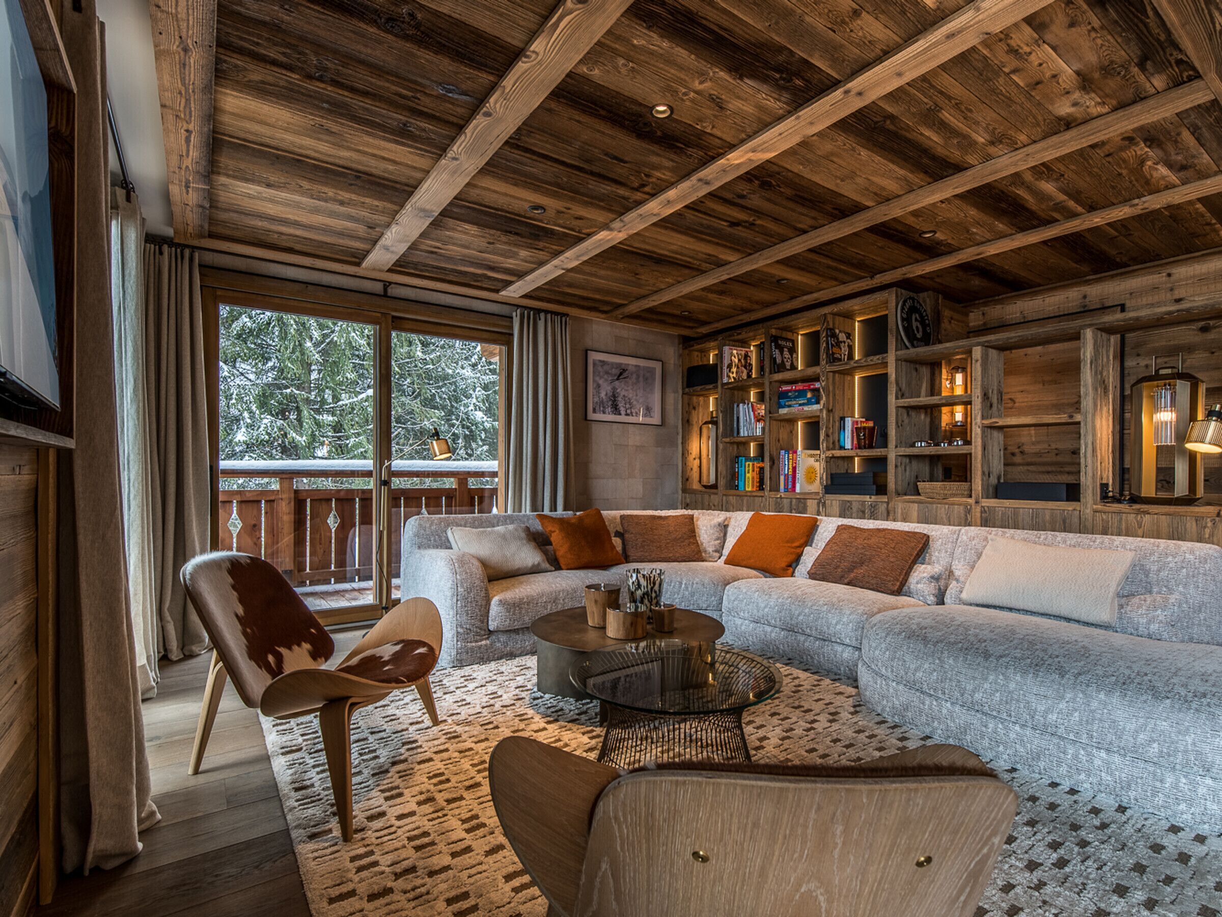 A cozy living room with a wooden ceiling, a large sofa, a coffee table, and a bookshelf filled with books.