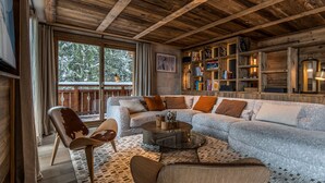 Un salon chaleureux avec un plafond en bois, un grand canapé, une table basse et une bibliothèque remplie de livres.
