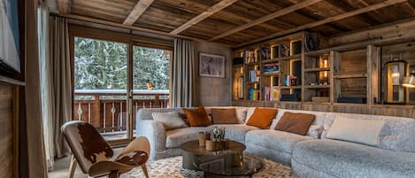 A cozy living room with a wooden ceiling, a large sofa, a coffee table, and a bookshelf filled with books.
