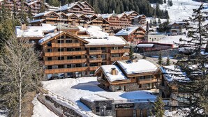 Une station de ski avec plusieurs bâtiments en bois, un panneau indiquant « Les Grands Chaëts des Pistes », et des montagnes enneigées en arrière-plan.