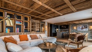 Un salon moderne doté d’un grand canapé d’angle, d’une table basse ronde et d’un coin repas avec un mur en pierre et des tabourets de bar.