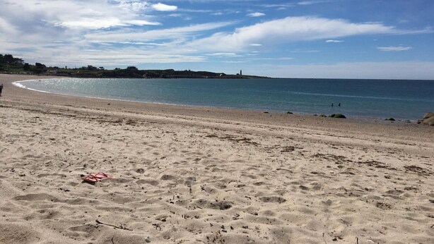 En strand med sandet bredde, en klar himmel og en bygning i det fjerne.
