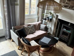 A living room with a sofa, a wicker chair, a round table, a lamp, a fireplace, and a window with curtains.