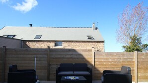 En udendørs patio med stenvæg, træterrasse og loungesæt i sort flet.