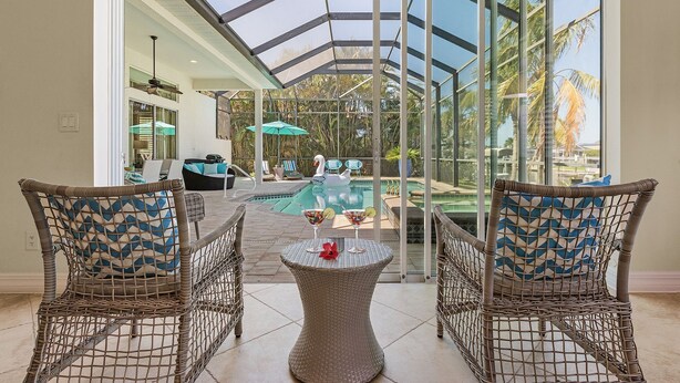 Eine verglaste Terrasse mit Korbmöbeln, einem Pool und Blick auf Palmen.