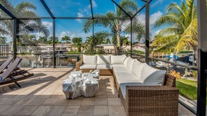 Ein sonnendurchfluteter Außenbereich mit Glasveranda, ausgestattet mit einem weißen Sofa, einem Korbstuhl und einem Marmortisch.