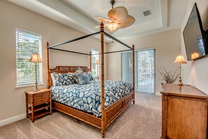 A four-poster canopy bed with a patterned bedspread, two bedside tables with lamps, a wooden dresser, and a large mirror on the wall. - Two homes that exude luxury and comfort, Heated Pools - Villa Blue Pavilion- Roelens Vacations (Cape Coral)