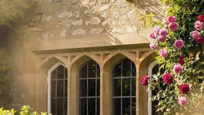 A stone building with three arched windows and a garden with pink flowers and green shrubs. - Weston Manor Hotel (Bicester)