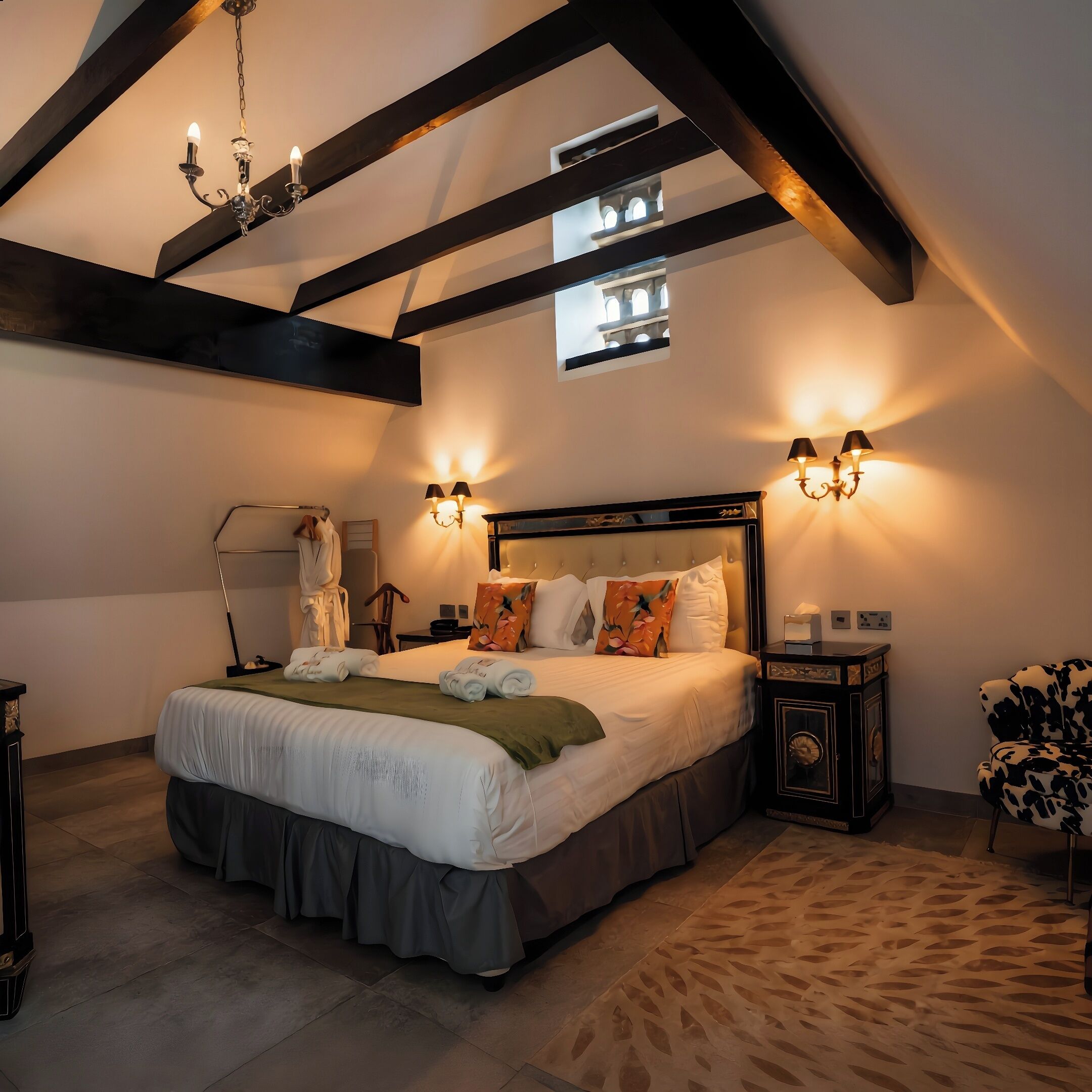 Une chambre à coucher avec un grand lit, un lustre, des appliques murales, un miroir et une petite fenêtre.
