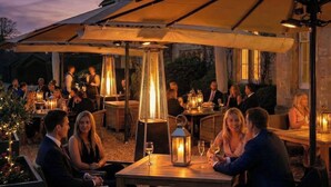 An outdoor dining area with tables and chairs, covered by umbrellas, and lit by lanterns. - Weston Manor Hotel (Bicester)