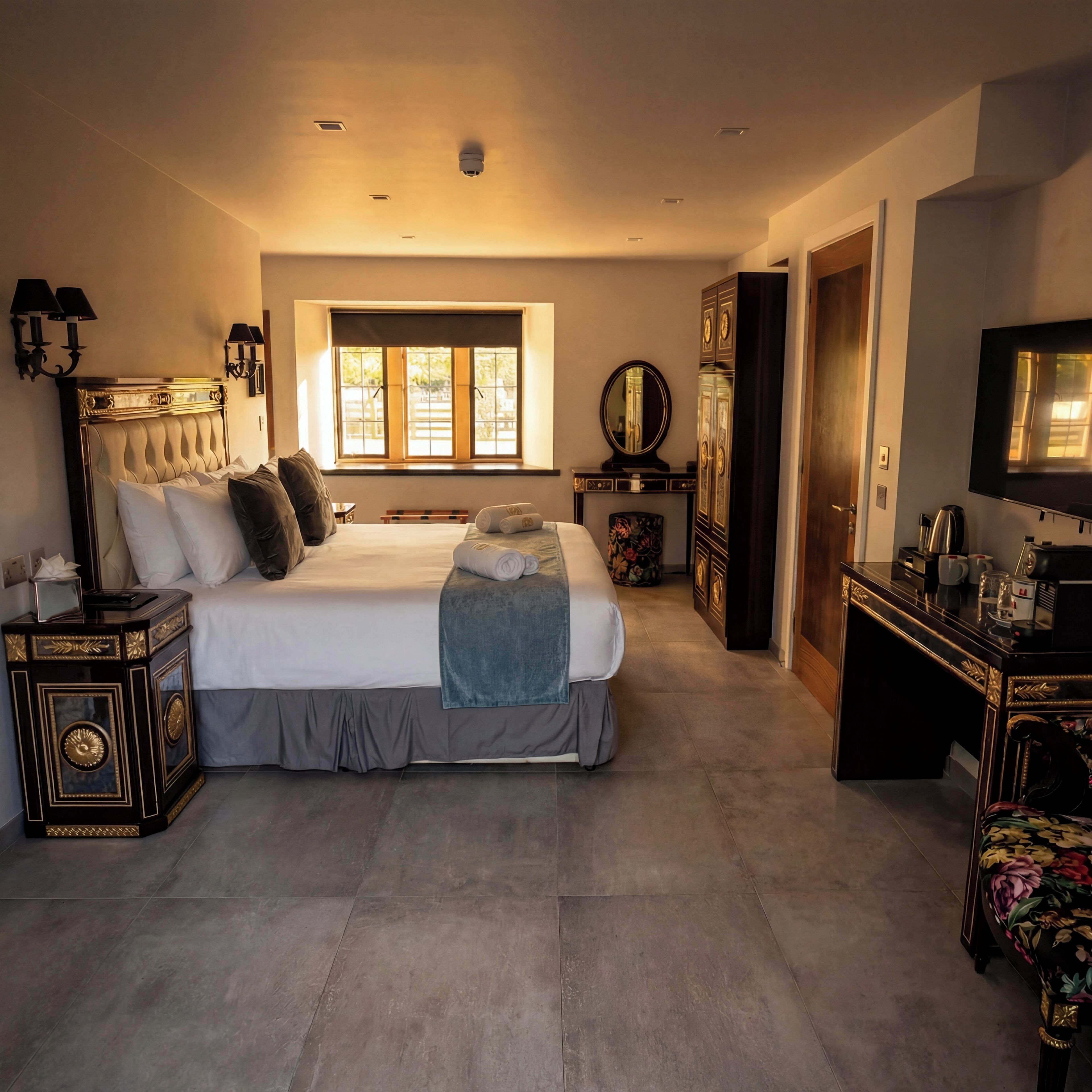 A spacious bedroom with a large bed, a dresser, a vanity, and a television.