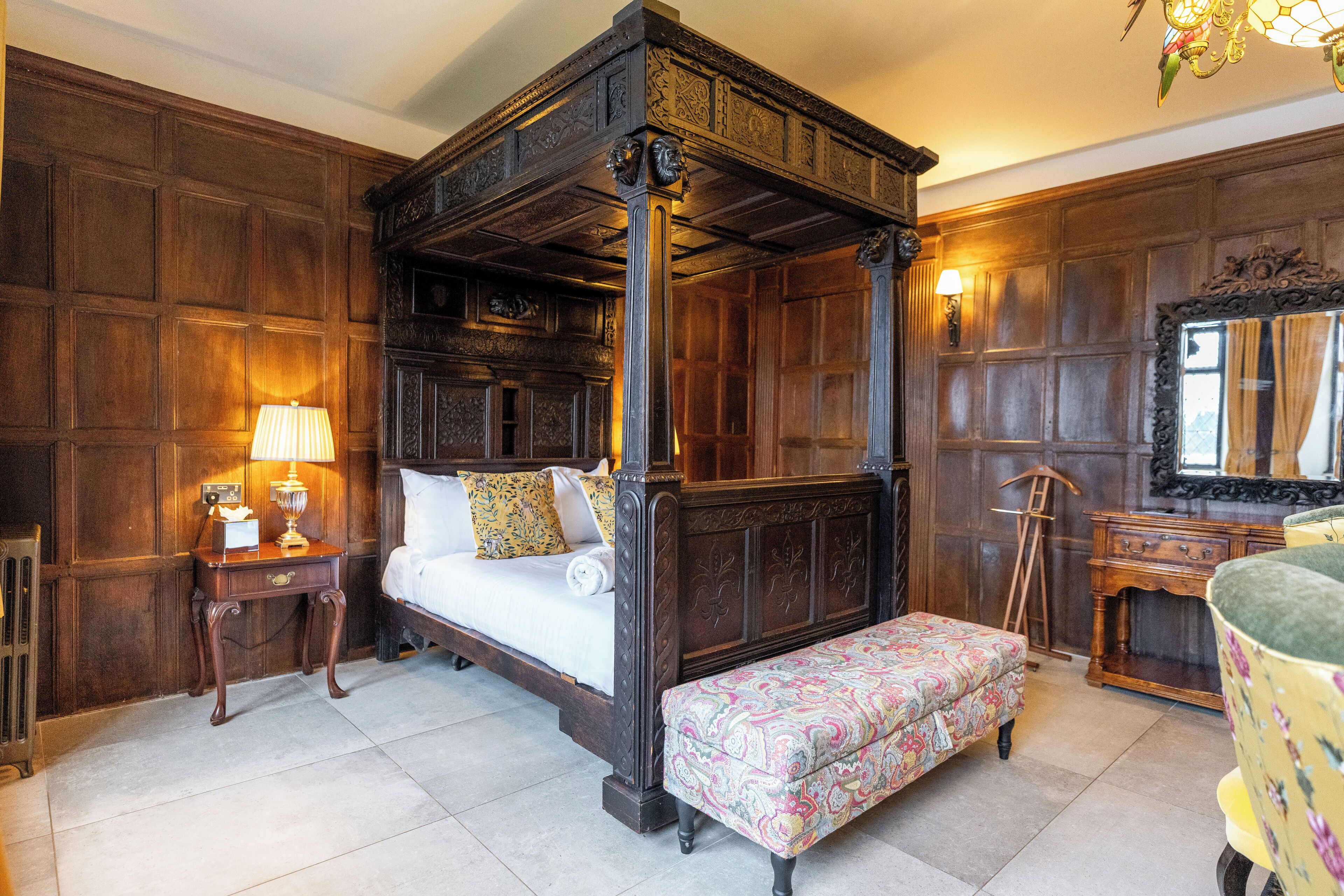 A four-poster bed with a matching bench, a bedside table with a lamp, and a mirror on the wall.