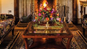 A room with a fireplace, a wooden table with a glass top, and a floral arrangement. - Weston Manor Hotel (Bicester)