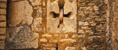 A stone wall with a square window featuring a decorative metal grille.