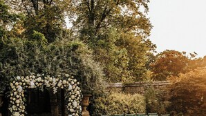 An outdoor wedding venue with rows of white chairs with green sashes, a floral archway, and lush greenery. - Weston Manor Hotel (Bicester)