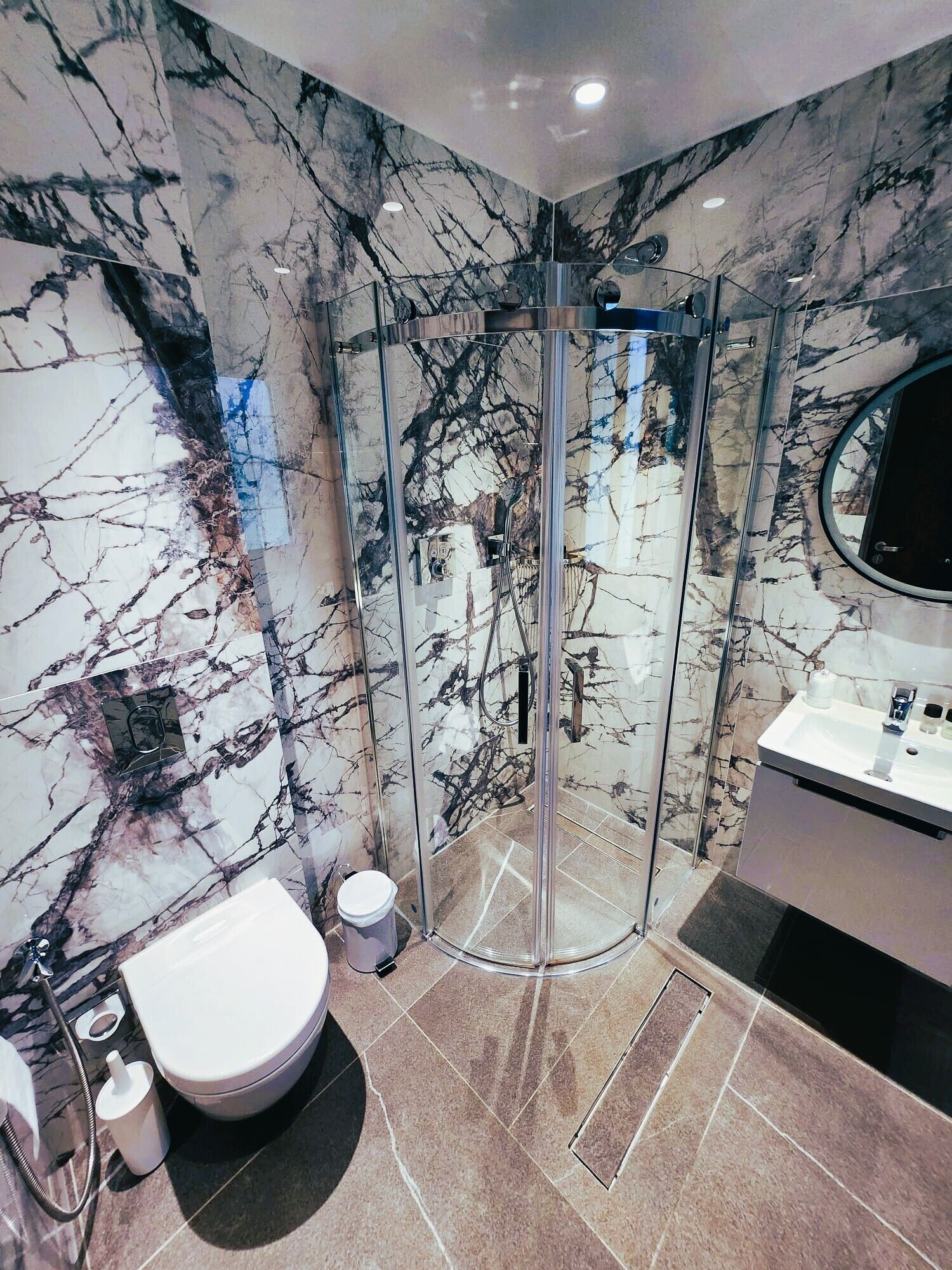 A modern bathroom with a glass-enclosed shower, marble walls, and a white sink.