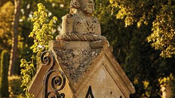Una estatua de piedra con tallas detalladas sobre un pedestal, rodeada por una cerca de hierro forjado.