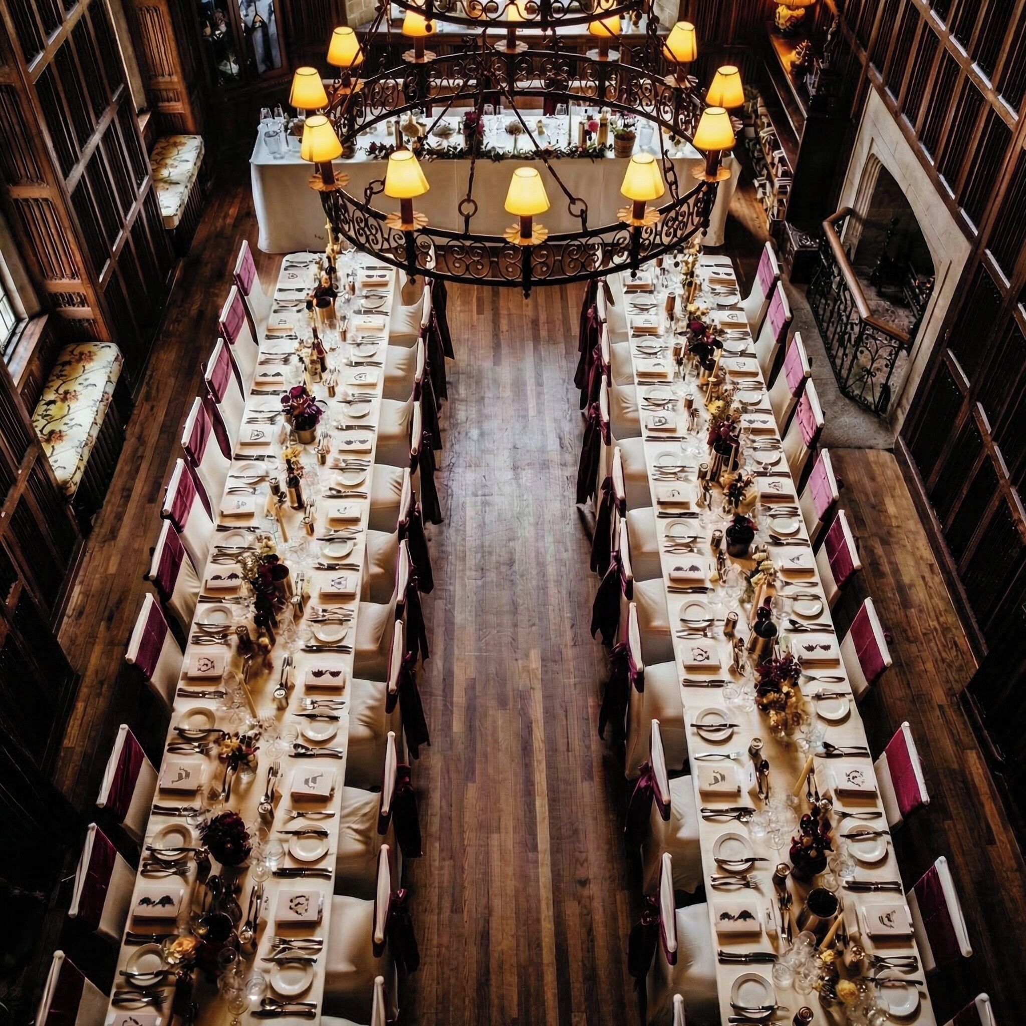 A long dining table with multiple chairs, surrounded by wooden walls and a chandelier.