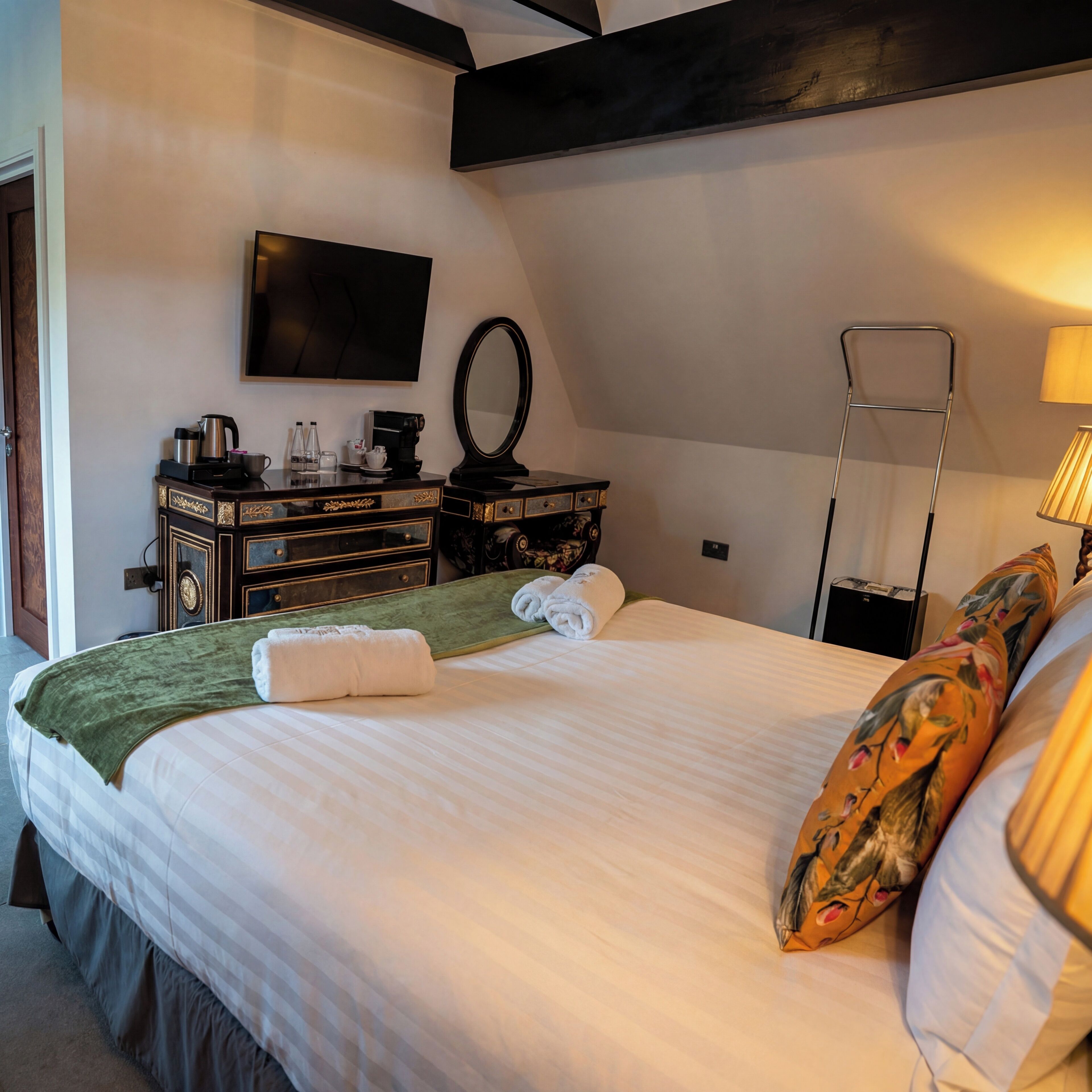 A hotel room with a bed, a flat-screen TV, a dresser, a mirror, a lamp, and a window.