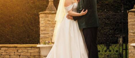 A couple embracing on stone steps with a stone balustrade and a hedge in the background.