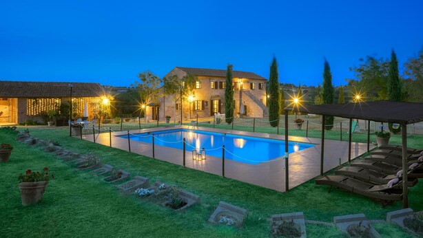 Ein Poolbereich mit Pool, Liegestühlen und einem Gebäude im Hintergrund, das beleuchtet ist.
